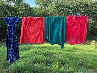 All four garments hanging on clothesline outdoors: blue floral brocade dress, two pink blouses, one teal blouse