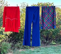 Front view of red dress, blue pants, plaid blouse hanging outdoors