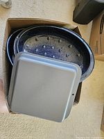 Box containing speckled enamel roaster parts and gray square cake pan