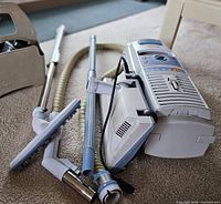 Canister vacuum with hose, wands and brush attachments on carpet