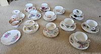 Fifteen saucers and twelve teacups arranged on carpet showing patterns and condition