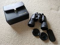 Binoculars, carrying case, lens caps and eyepiece cover on carpet