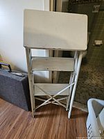 Folding white metal step stool folded against wall
