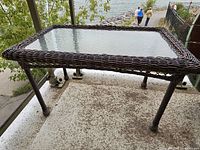 Full view of rectangular resin wicker patio table showing glass top and legs