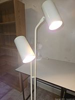 Full view of white metal floor lamp with two cylindrical shades illuminated
