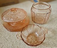 Group shot of all pink glass pieces: jar, lidded dish on plates, handled bowl