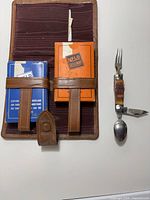 Leather case holding two card decks, folding camp utensil beside