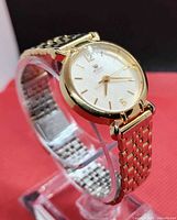 Left three-quarter view showing gold-tone case, white dial, bracelet links