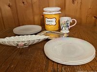 Group shot showing all items: stack of Petal plates, cookie jar, serving dish, metal tray, mug