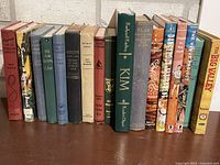 Row of ~19 assorted vintage hardcover novels on shelf