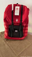 Front view of red Herschel Little America backpack with black straps and tags attached