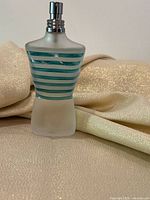 Full view of torso-shaped frosted glass bottle with teal stripes standing upright