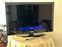 Front view of Toshiba television on stand with screen powered showing "No Signal" message, remote and small device on table