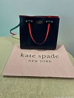 Front view of navy Kate Spade handbag on branded paper bag