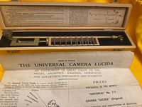 Open wooden case showing brass camera lucida, slide holder and paperwork