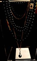 Multiple necklaces and pendant displayed on stand showing strands, clasp and pearl pendant