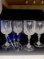 Four cut crystal wine glasses, three blue-top bottle stoppers in stainless holder against dark background