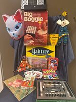Group shot of all items including Big Boggle, Yahtzee, Autobridge, card decks, crayons, dominoes, wooden toys, UNO deck, cat mask