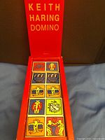 Open red wooden box showing first nine Keith Haring domino tiles