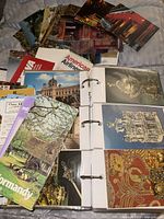 open binder showing pages with multiple postcards and pile of additional postcards and brochures