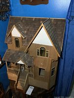 Front angled view of complete wooden dollhouse showing roof, porch, windows