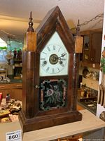 Front view of wooden steeple clock showing dial and floral glass panel