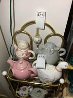 Overview of four teapots on top shelf of brass cart