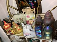 Shelf containing ceramic rooster teapots, porcelain vases, iridescent art glass pieces and compotes