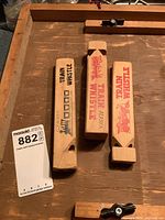 Three wooden train whistles on table with lot tag, showing graphics and size