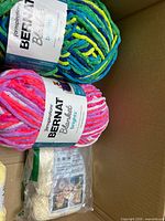 Top view of two Bernat Blanket Brights skeins and sealed off-white yarn in box
