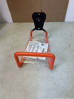 Full view of orange metal hose holder with black mounting plate