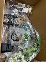 Top view of box showing black metal stand parts, wire cage, bagged green succulents, white hydrangea cluster