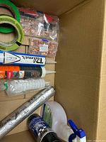 Box interior showing green tape, copper terminals, sealant tubes, flashing tape, spray bottle