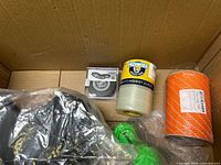 View of box showing tape roll, nylon rope spool, garden line spool, black disc in case, bagged item