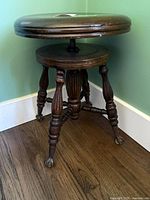 Full view of piano stool showing round seat, central screw, turned legs, and claw feet