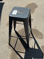 Overall view of dark gray metal bar stool showing seat, legs and tag