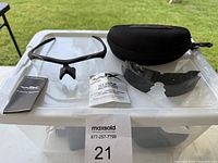 Full set showing glasses frame with clear lens, spare grey lens, case and manuals