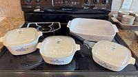 Three lidded square casseroles, handled skillet, rectangular roaster on stovetop