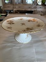 Round pedestal cake plate showing gold floral decoration and pleated pedestal