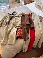 Three coats laid out: beige trench, brown alpaca coat, cream patterned coat with red lining
