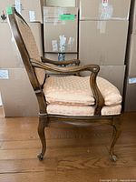 Side profile of one armchair showing carved wood frame, cabriole legs, arm shape and upholstery