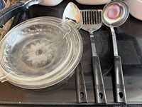 Two starburst glass lids and three black-handled utensils on stovetop
