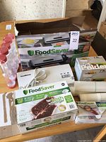 Overview of boxed FoodSaver units, bag rolls, bags, scale, and jars on table