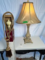 Lamp and boxed drapery rod with tassel on table