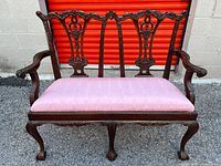 Front view of carved wood settee with pink seat