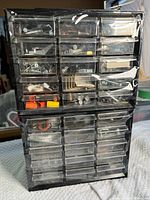 Front view of black plastic organizer with multiple clear drawers, some holding assorted screws and hardware