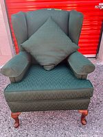 front view of green wingback chair with pillow and arm protectors