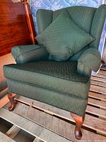 Front view of green wingback chair with pillow, wooden cabriole legs visible