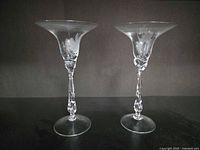 Two clear crystalline champagne coupes showing etched floral motif, twisted stems and flared bowls