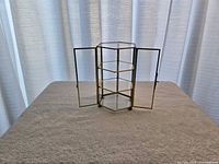 Hexagonal brass and glass case with doors open, showing shelves